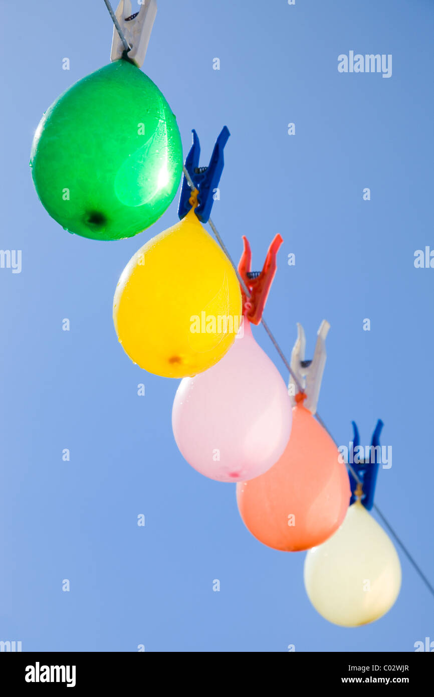 Selective focus on a colored bunch of balloons with water-drops hanging on a clothesline with a blue sky as background Stock Photo