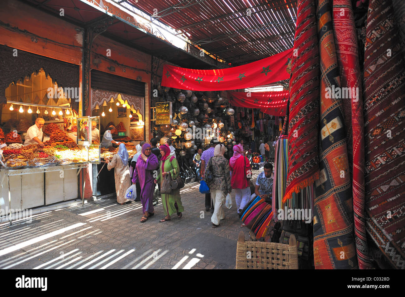 Street in the souk market, bazaar in the Medina of Marrakech, a trader hanging out his wares, opposite, a vendor sweets Stock Photo