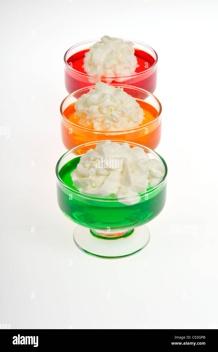 Orange, strawberry and lime Jell-O with whipped cream topping in glass serving dishes on white background, cutout. Stock Photo