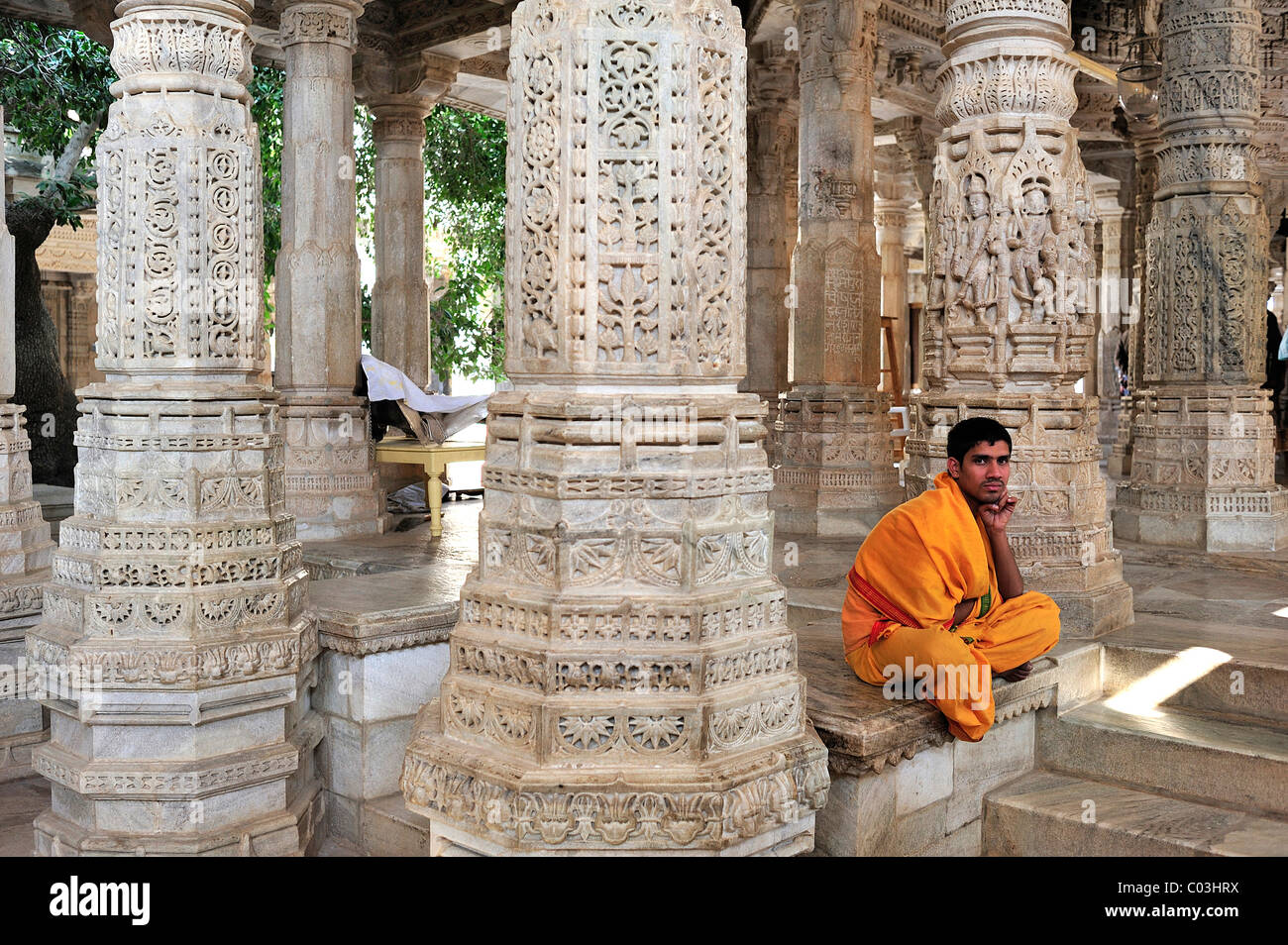 Young monk wearing the traditional yellow monk's robe in the inner hall with ornate marble pillars in the Temple of Ranakpur Stock Photo