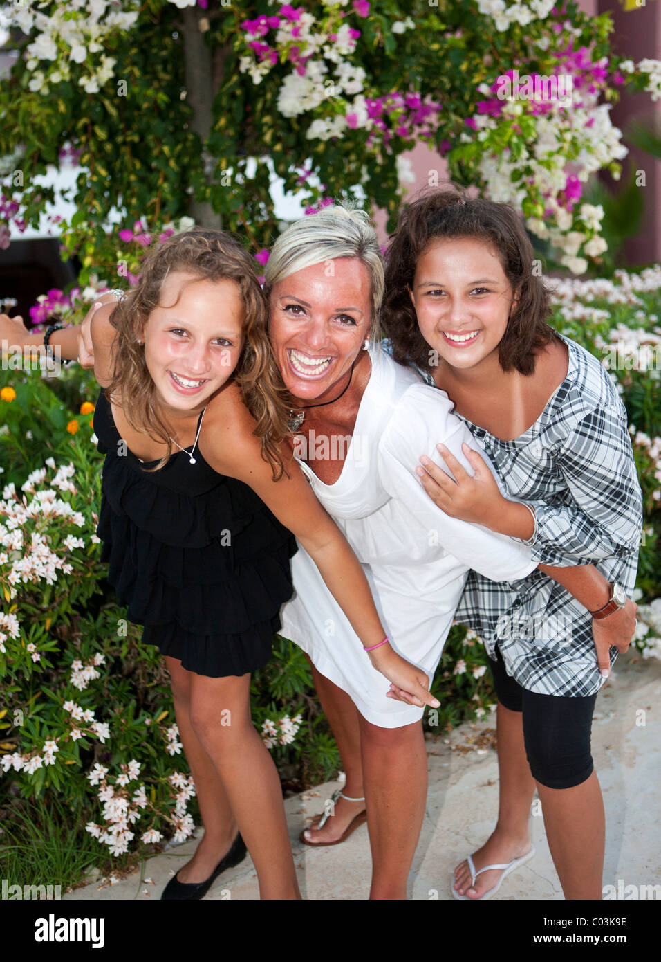 Portrait of a mother with two thirteen-year-olds girls in front of flowers Stock Photo