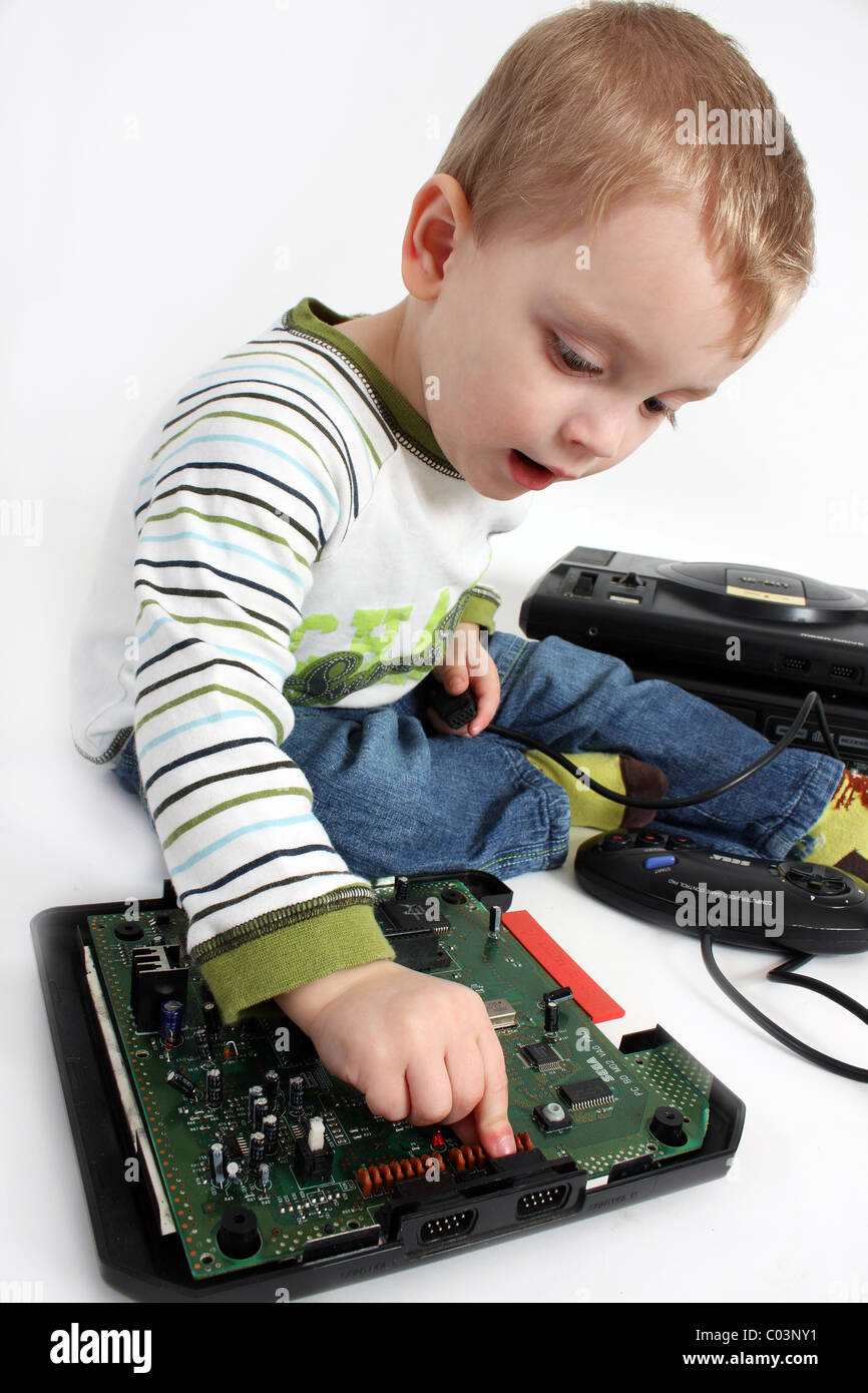 An inquisitive young toddler boy opening up a Sega Mega Drive retro gaming console and looking inside to see how it works Stock Photo