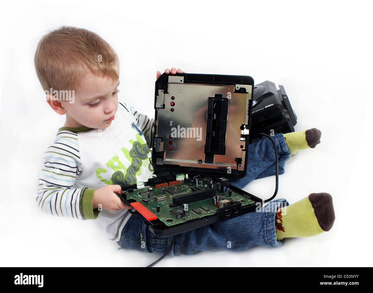 An inquisitive young toddler boy opening up a Sega Mega Drive retro gaming console and looking inside to see how it works Stock Photo