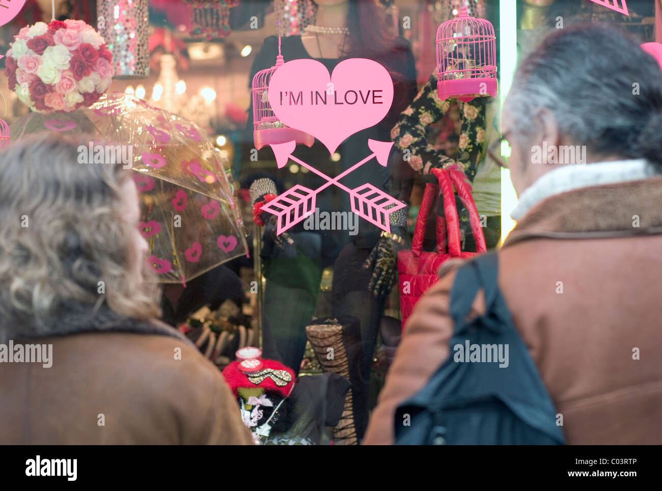 Couple looking into a store window with a pink heart sticker saying 'I'm in Love' Stock Photo