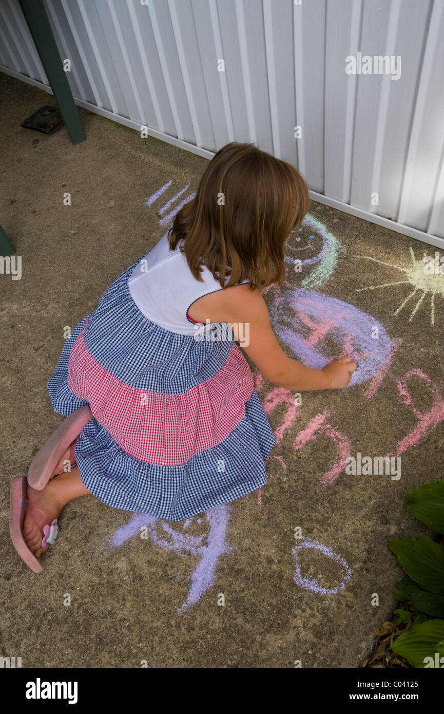 Young girl drawing name with chalk on sidewalk. Stock Photo