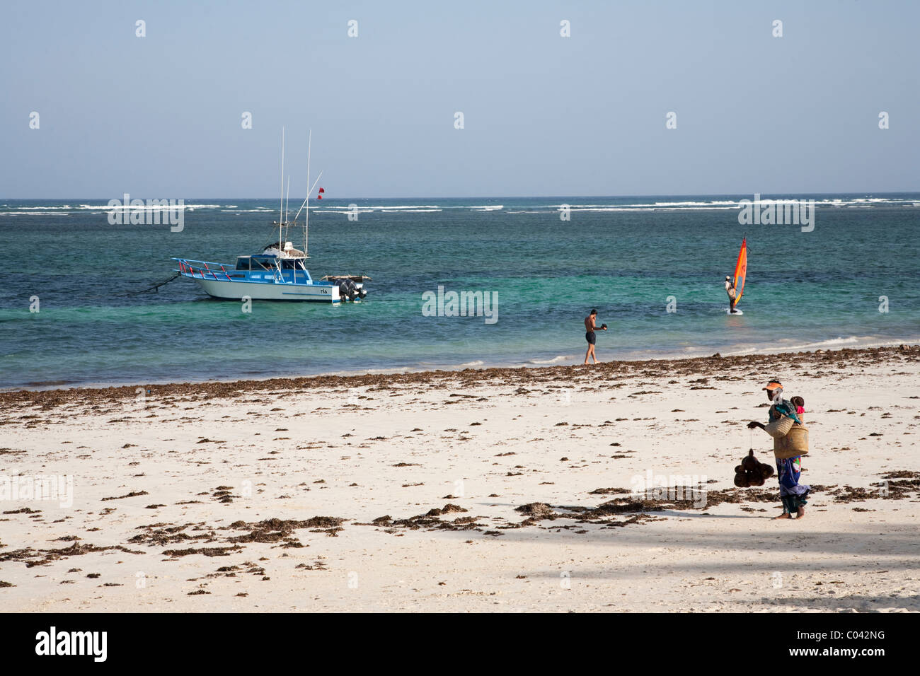 Woman selling gourds, with a baby strapped to her back is walking on Diani beach waiting for tourists, Kenya Stock Photo