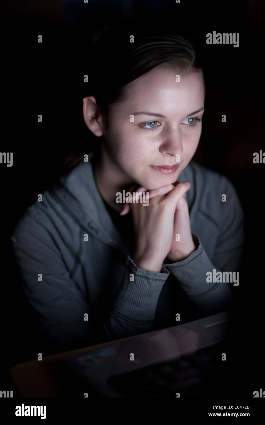 Teenager looking at computer screen in a darken living room Stock Photo