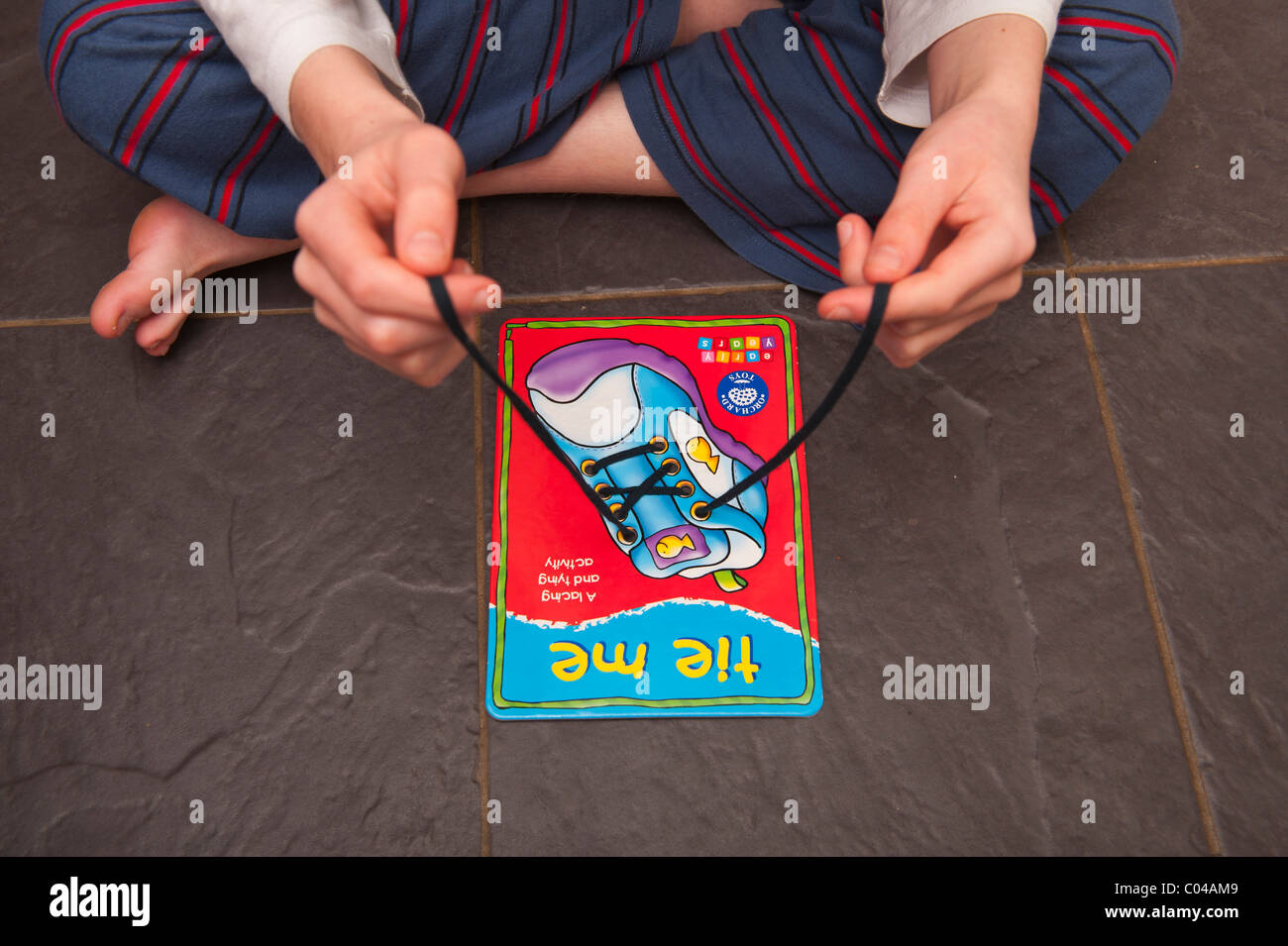 A MODEL RELEASED boy practises tying shoelaces on a learning card by orchard toys in the Uk Stock Photo