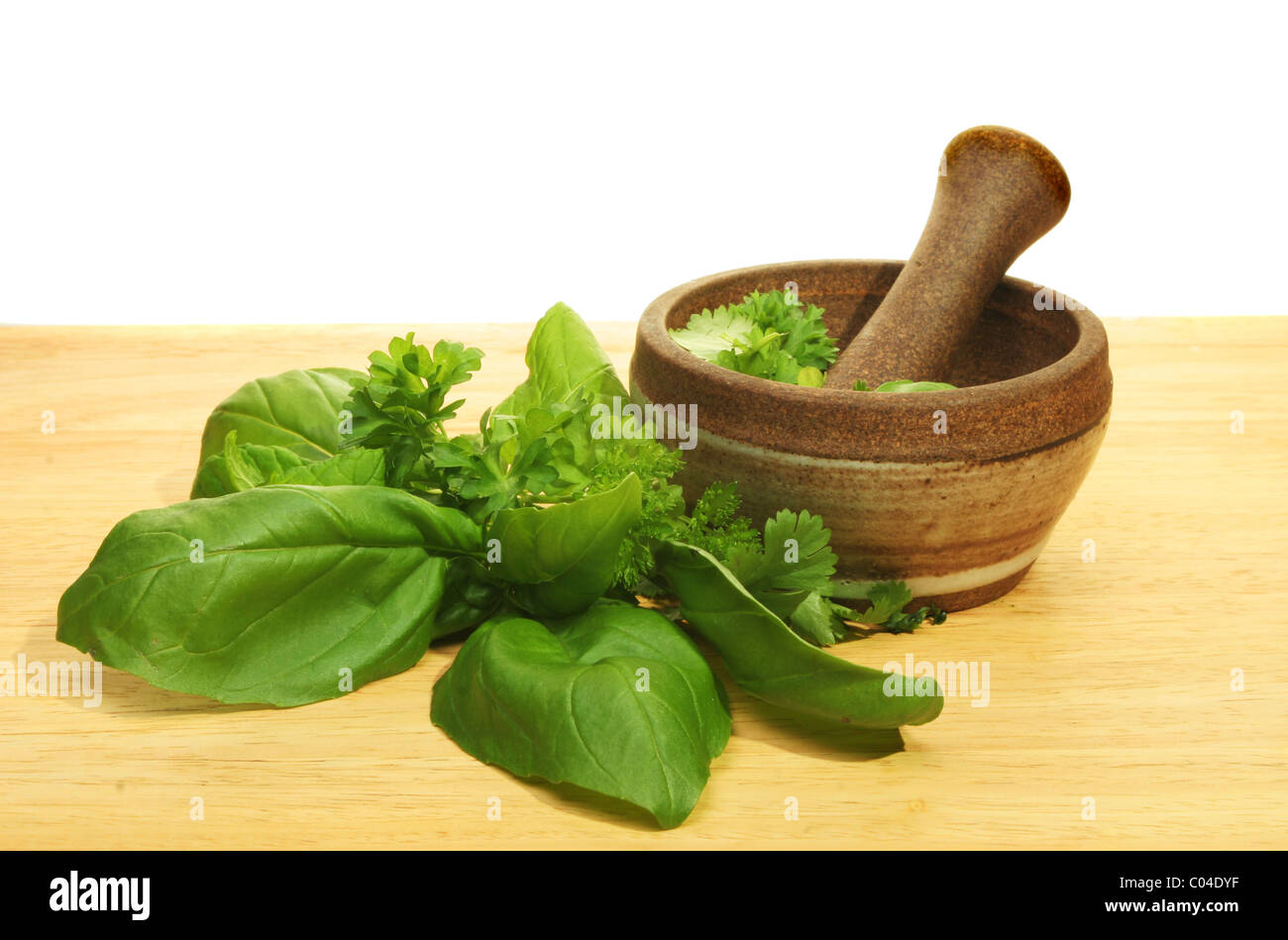 Pestle and mortar with fresh herbs on a wooden board Stock Photo