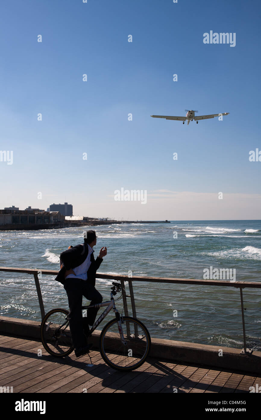 Young male bike rider smoking and watching a plane come in for landing at Sde Dov Hoz Airport in Tel-Aviv Stock Photo