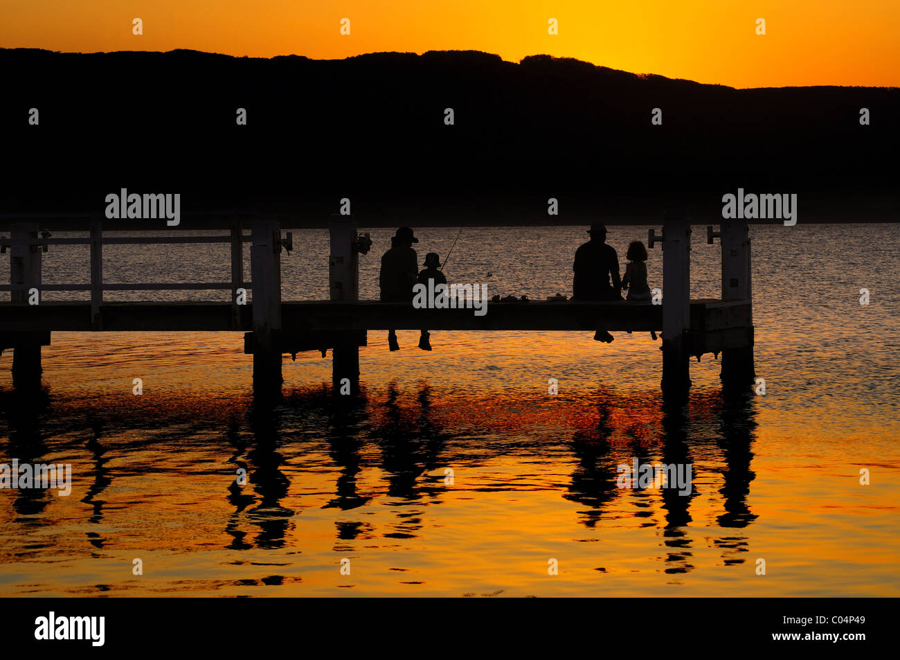 A family fishing from the jetty in Lake Illawarra at sunset, NSW