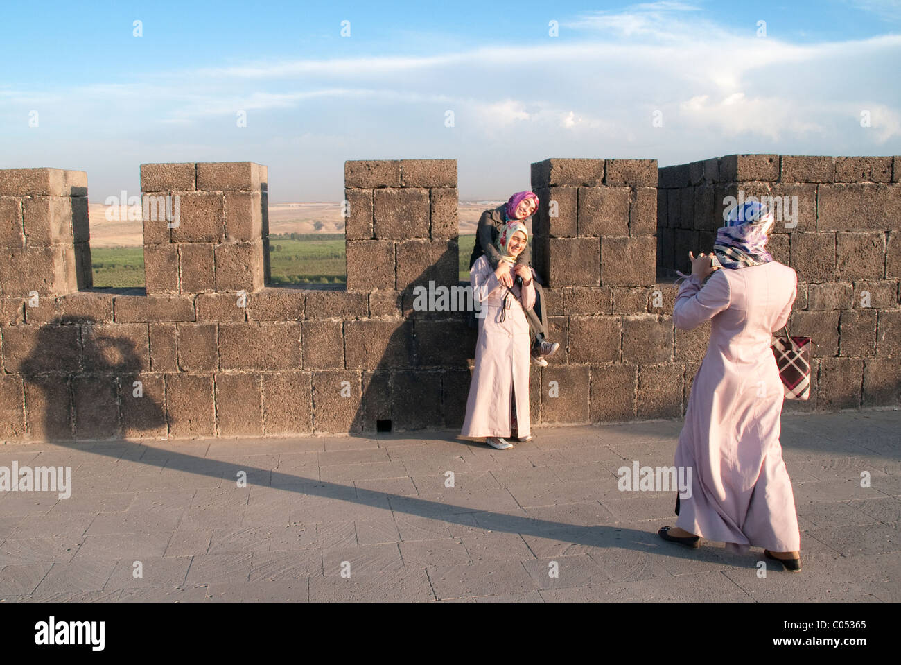 Three young Kurdish women in hijab taking a photo atop the old walls and fortress of the city of Diyarbakir, in eastern Anatolia, southeastern Turkey. Stock Photo