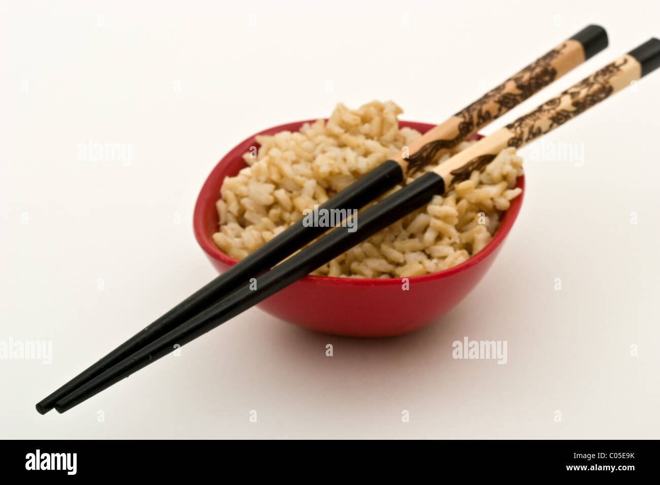 Red bowl of brown rice with black ornamental chop sticks on top Stock Photo