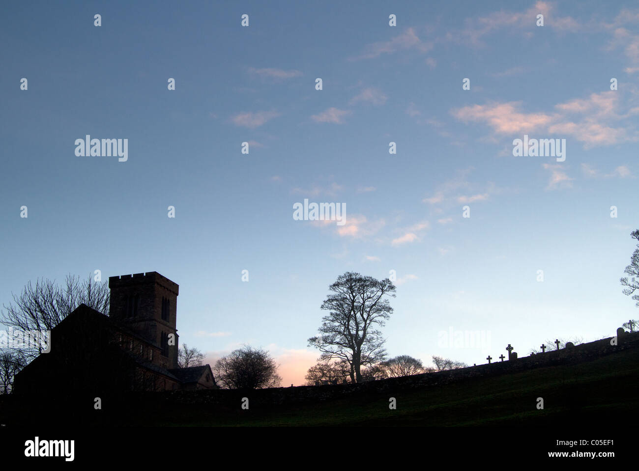 A church with head stones silhouetted against a blue sky Stock Photo