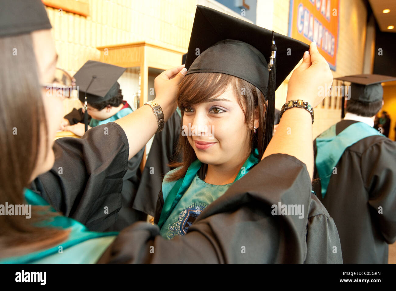 Hispanic teenage girl adjusts friend's mortarboard before high school graduation ceremony in El Paso Texas USA Stock Photo