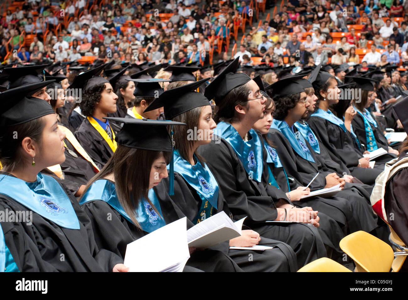 High school seniors in caps and gowns sitting in a row wait to receive