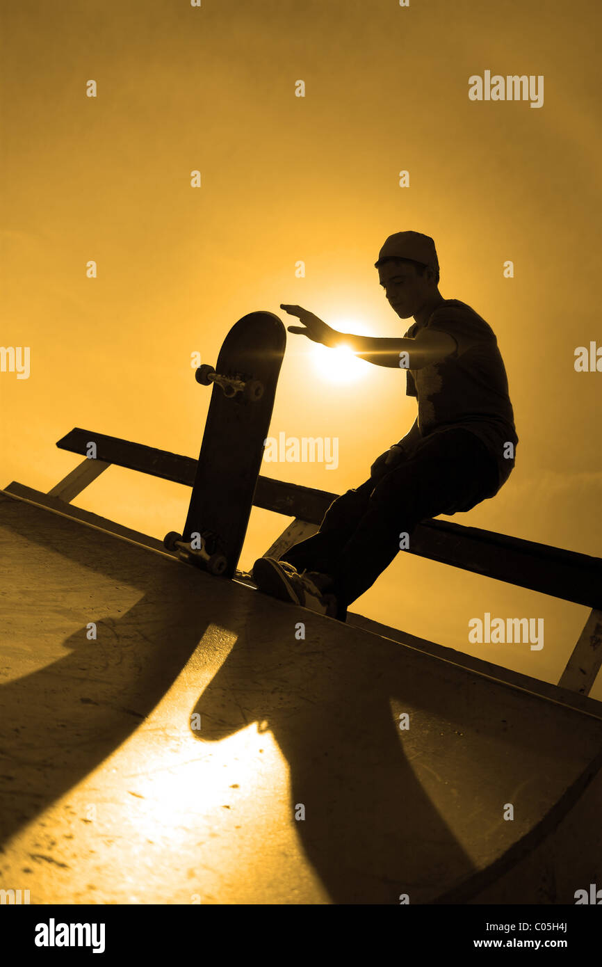 A silhouette of a young skateboarder at the top of a ramp at the skate park. Stock Photo