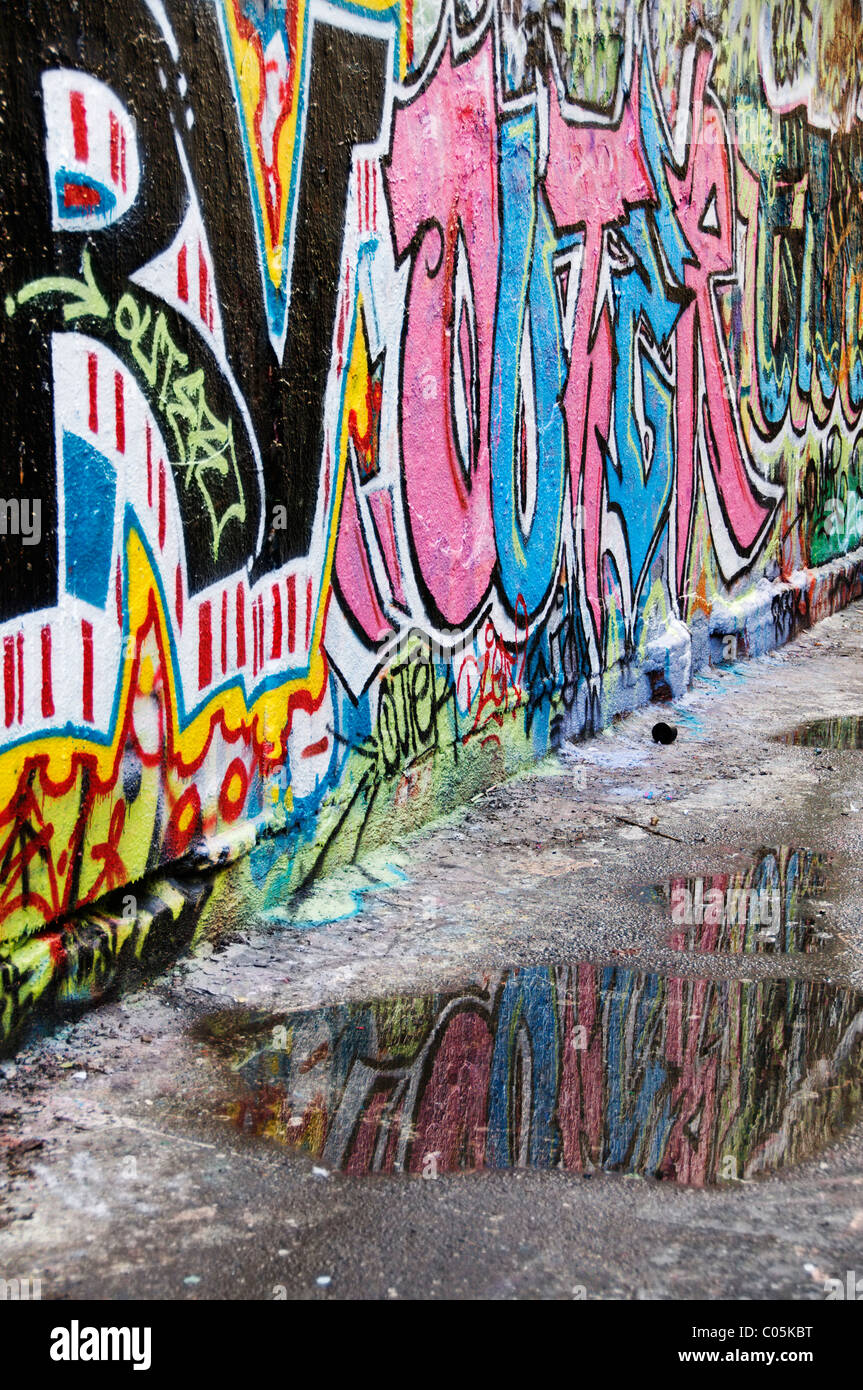 Vertical view of Capitol Theater's Free Wall behind the building painted with colorful graffiti and reflected in an alley puddle Stock Photo