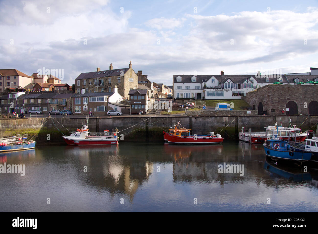 The harbour at Seahouses with the 'Bamburgh Castle' Inn on the quayside and moored boats at low tide Stock Photo