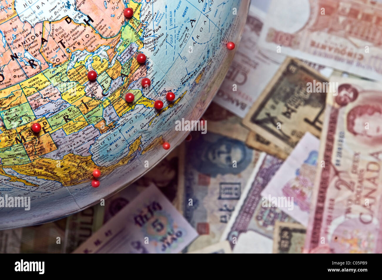 A globe, above world currency, with pins in it to show places traveled. Stock Photo