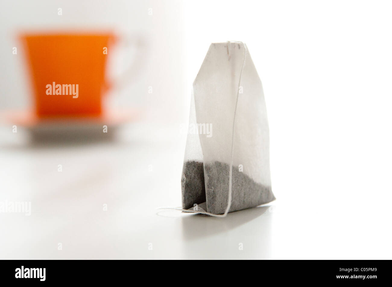 close up of tea bag with out of focus orange tea cup in background Stock Photo