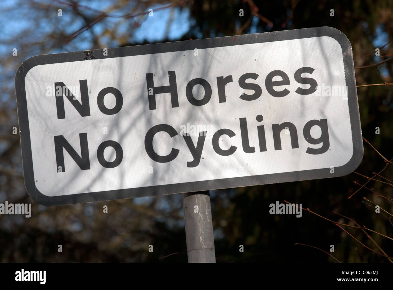 A sign saying 'No Horses, No Cycling' on a British village public footpath. There is a shadow from a nearby tree. Stock Photo