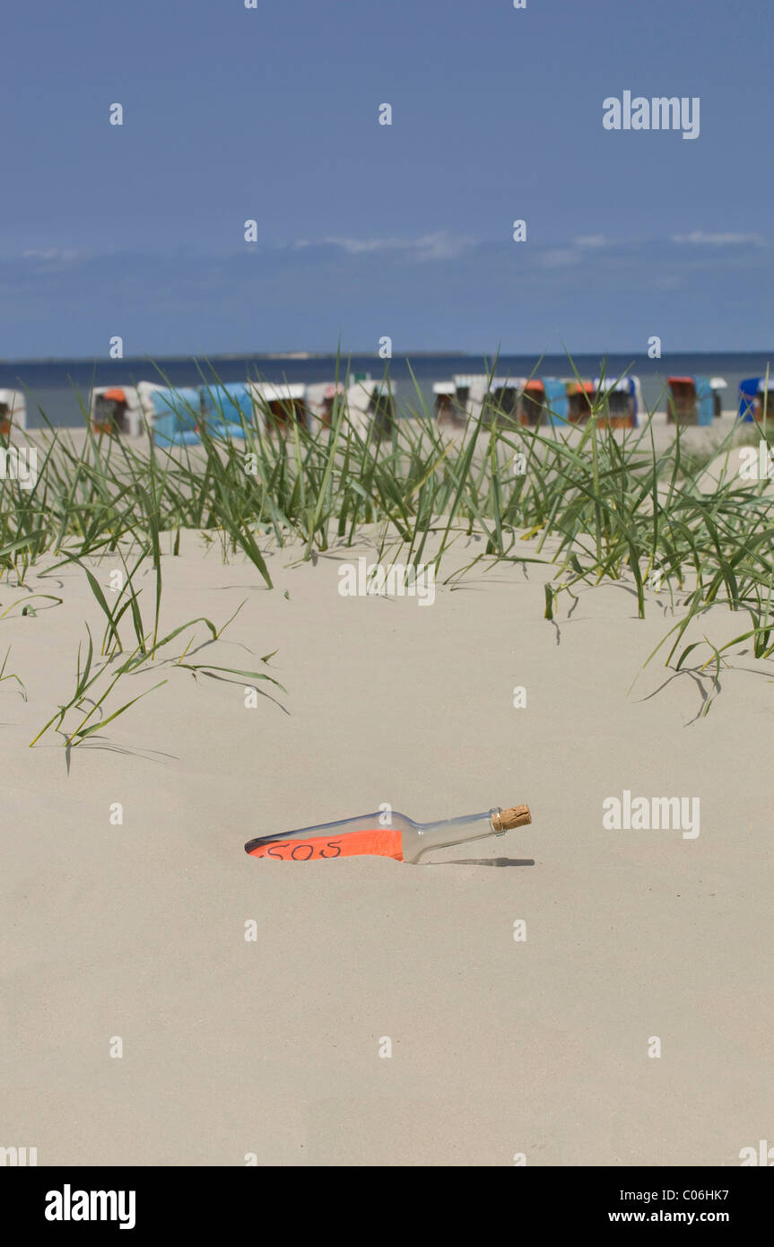 Stranded bottle with a SOS message on a sand dune in front of roofed wicker beach chairs and the North Sea, Norddeich, Norden Stock Photo