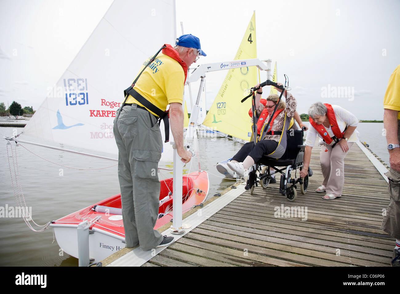 Sailing instructor with the Waveney Sailability Trust helps disabled woman into sailing dinghy using an Oxford Dipper Stock Photo