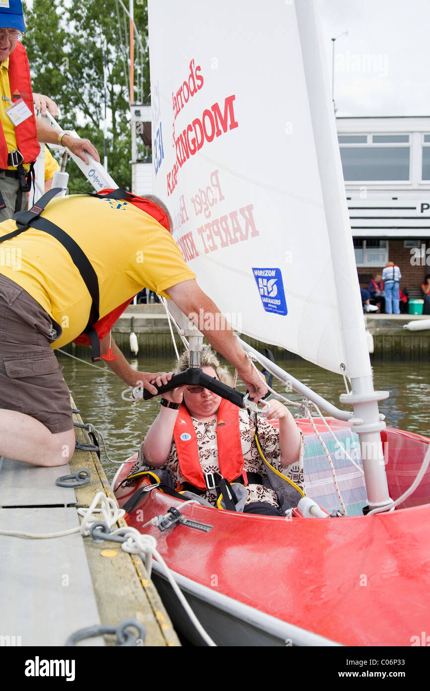Sailing instructor with the Waveney Sailability Trust helps disabled woman into sailing dinghy Stock Photo