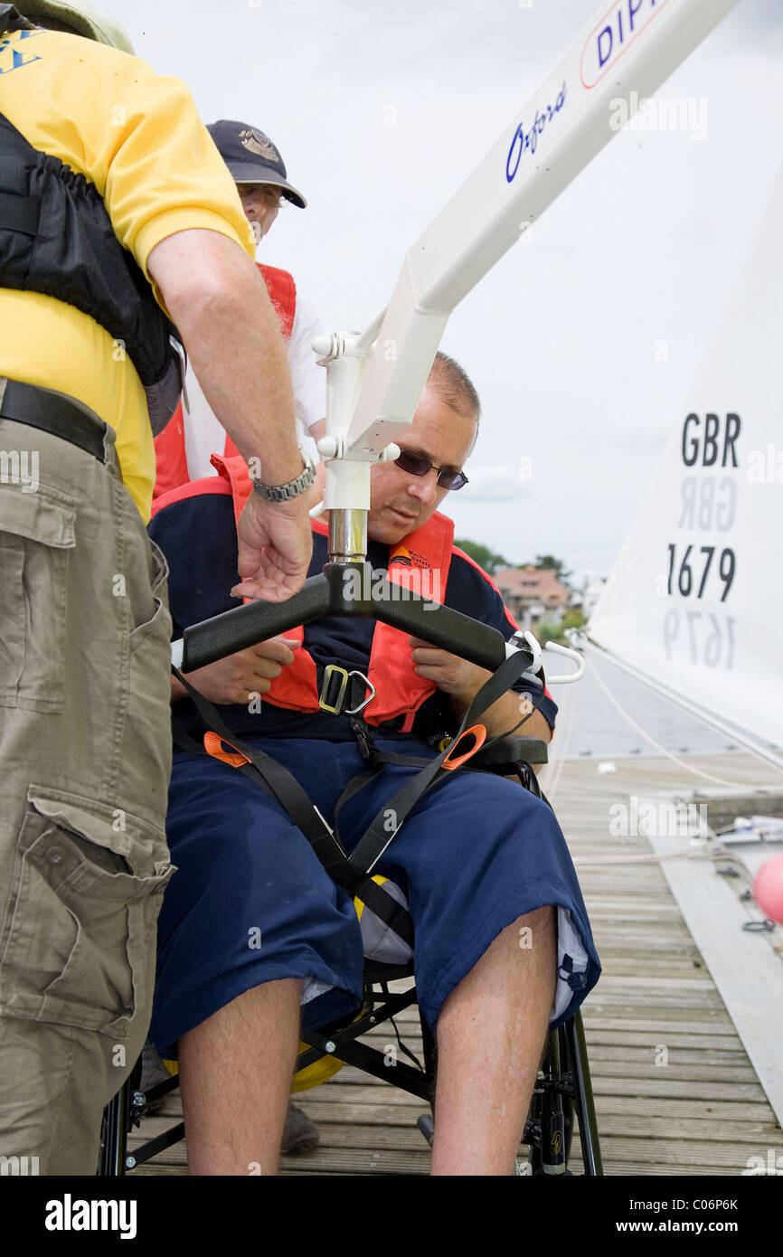 Sailing instructor helps disabled man into sailing dinghy using poolside hoist Stock Photo