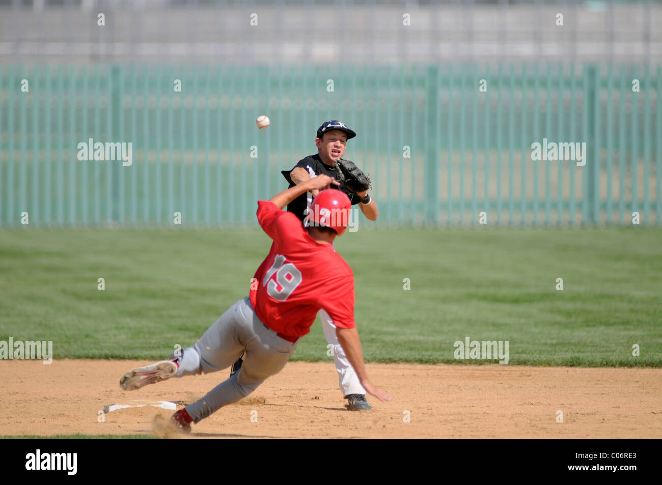 high school baseball game runner slides in as Second baseman throws
