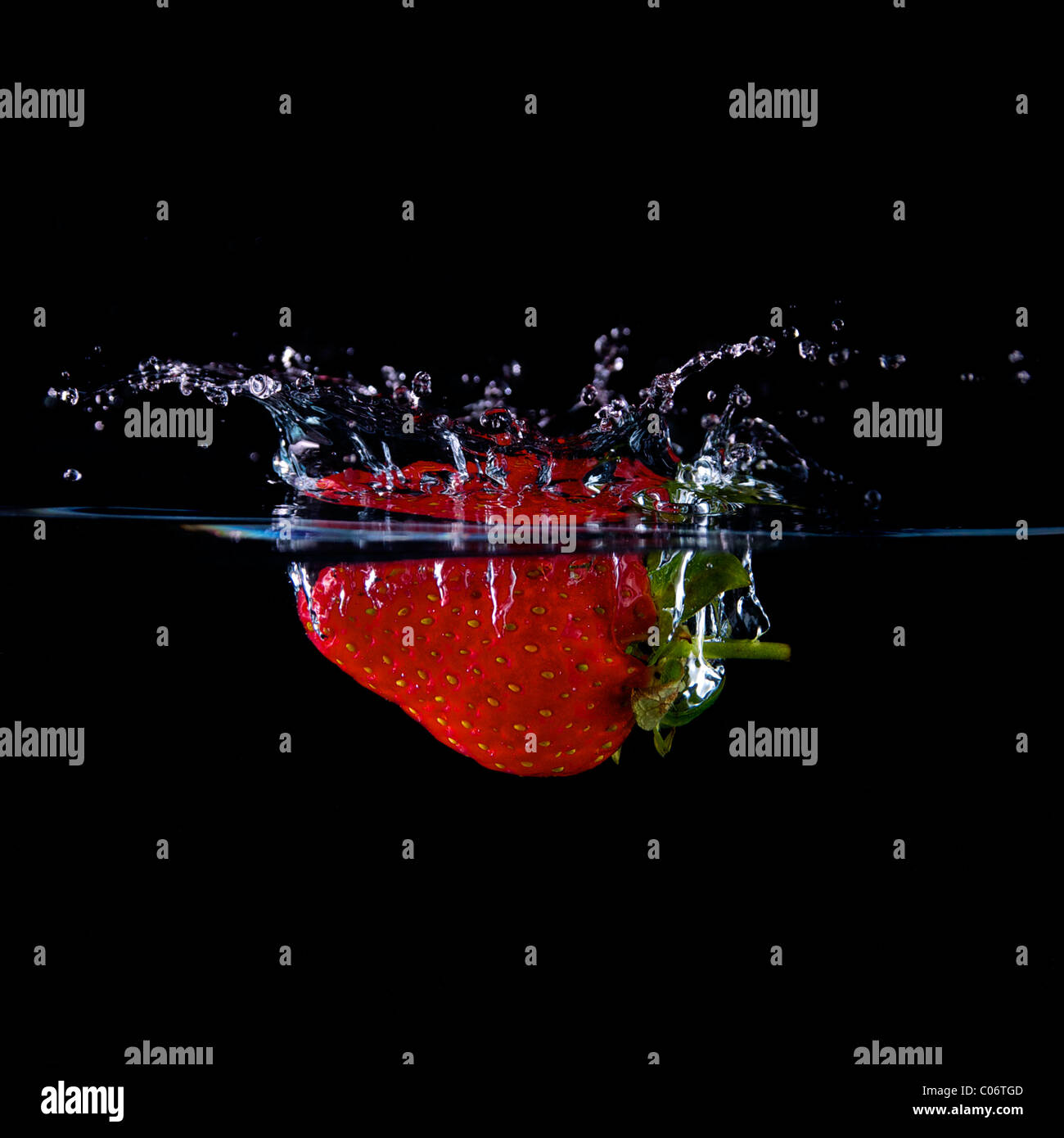 A Strawberry dropped into water creating a splash with black background Stock Photo