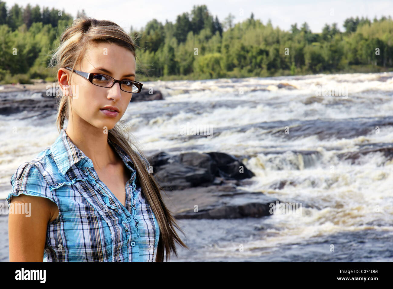 Young friendly brunette looking at camera in front of beautiful white waters waterfall landscape. Stock Photo