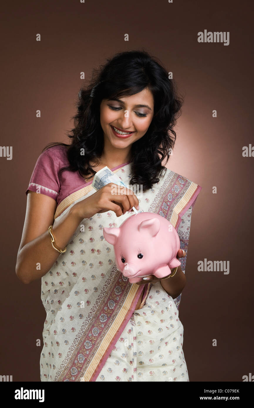 Woman putting a currency note into a piggy bank Stock Photo - Alamy