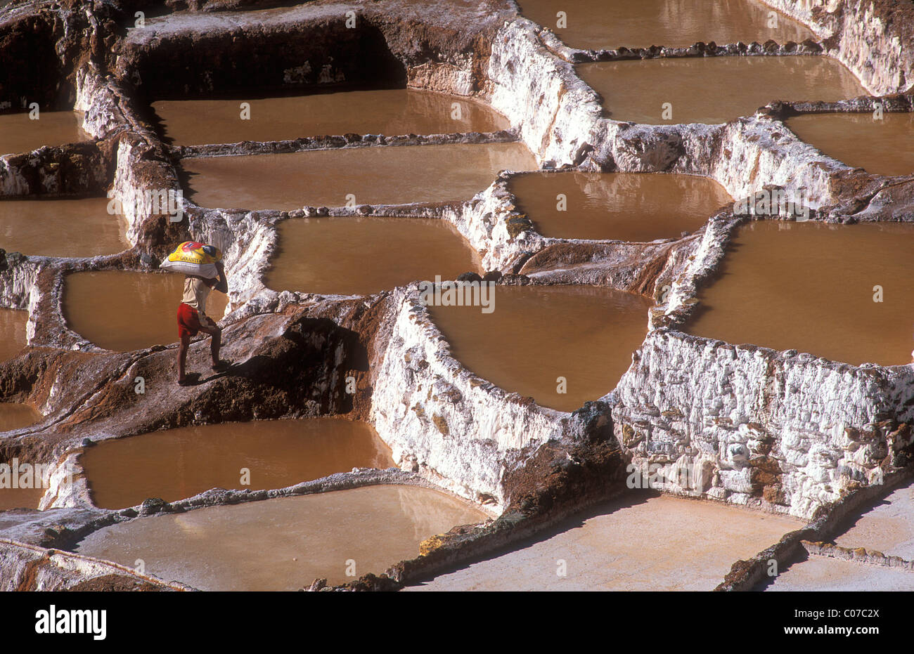 Salt terraces on a hillside at Pichingote, salt production by evaporation, a worker carries a