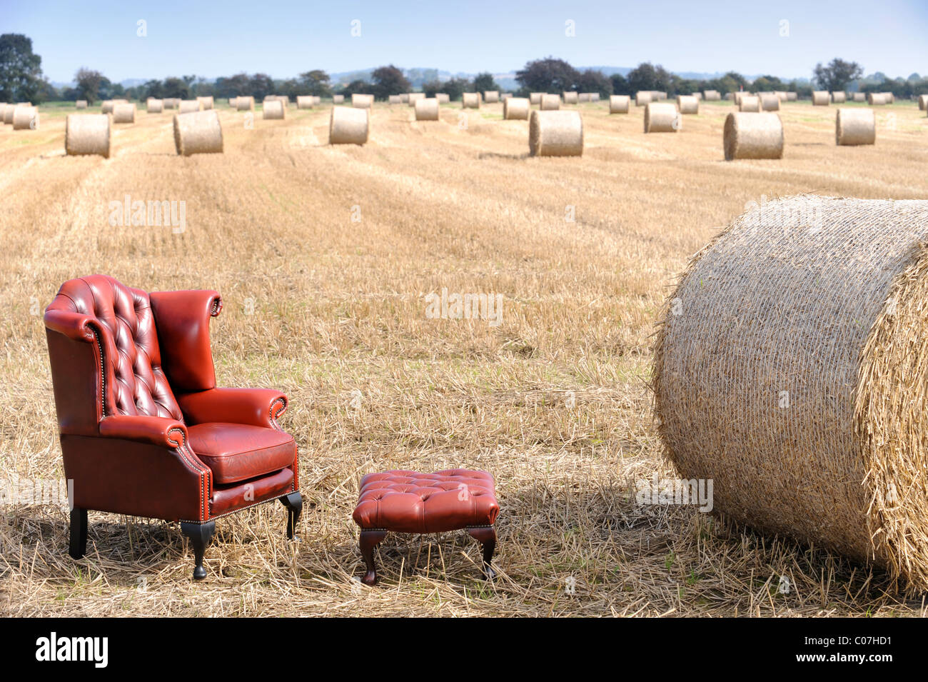 An antique red leather armchair in a field of harvested hay UK Stock Photo