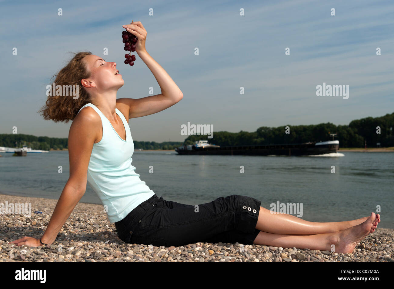 Young woman sitting on the riverbank eating grapes Stock Photo - Alamy