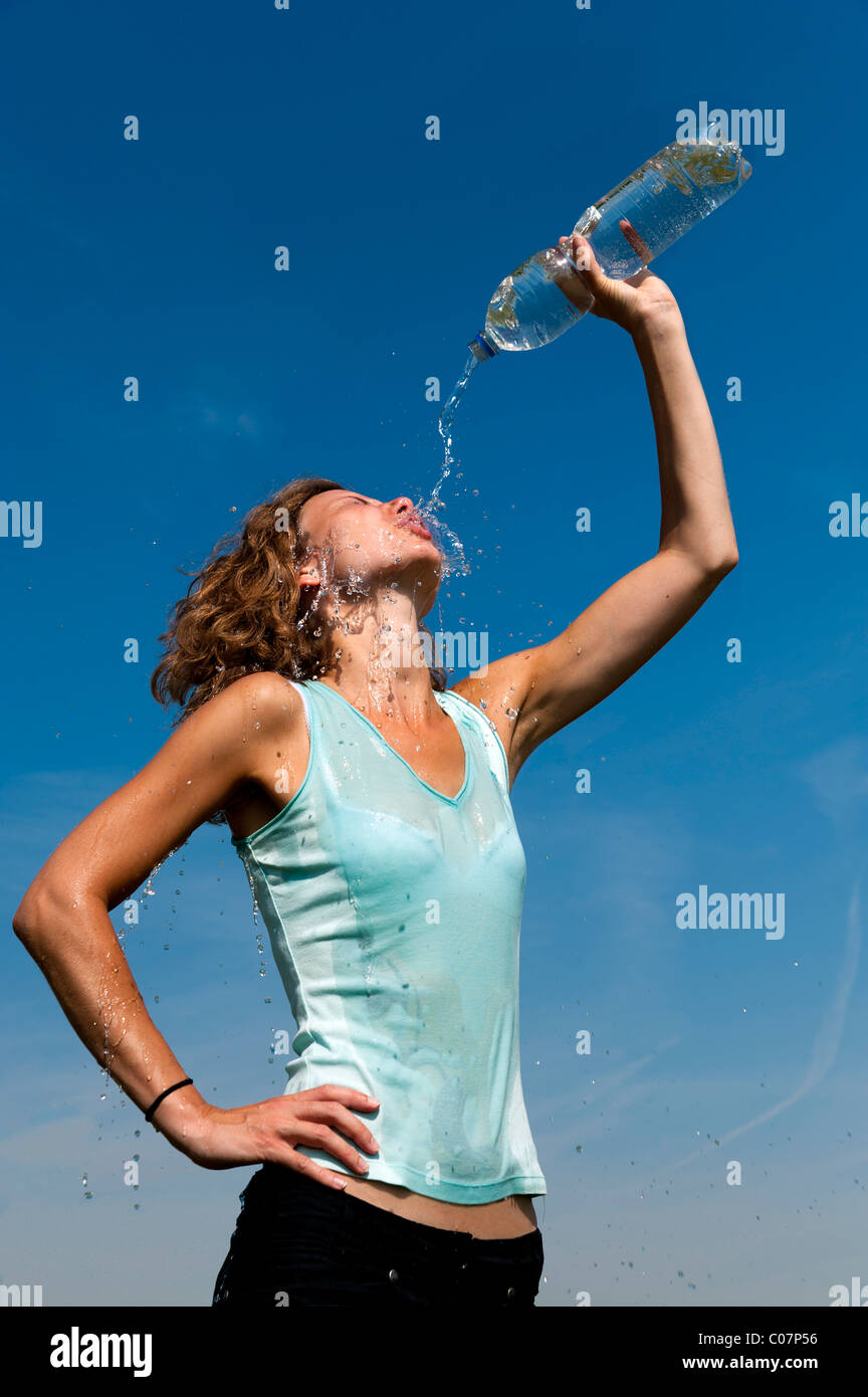 Young woman pouring the contents of a water bottle over her face Stock Photo
