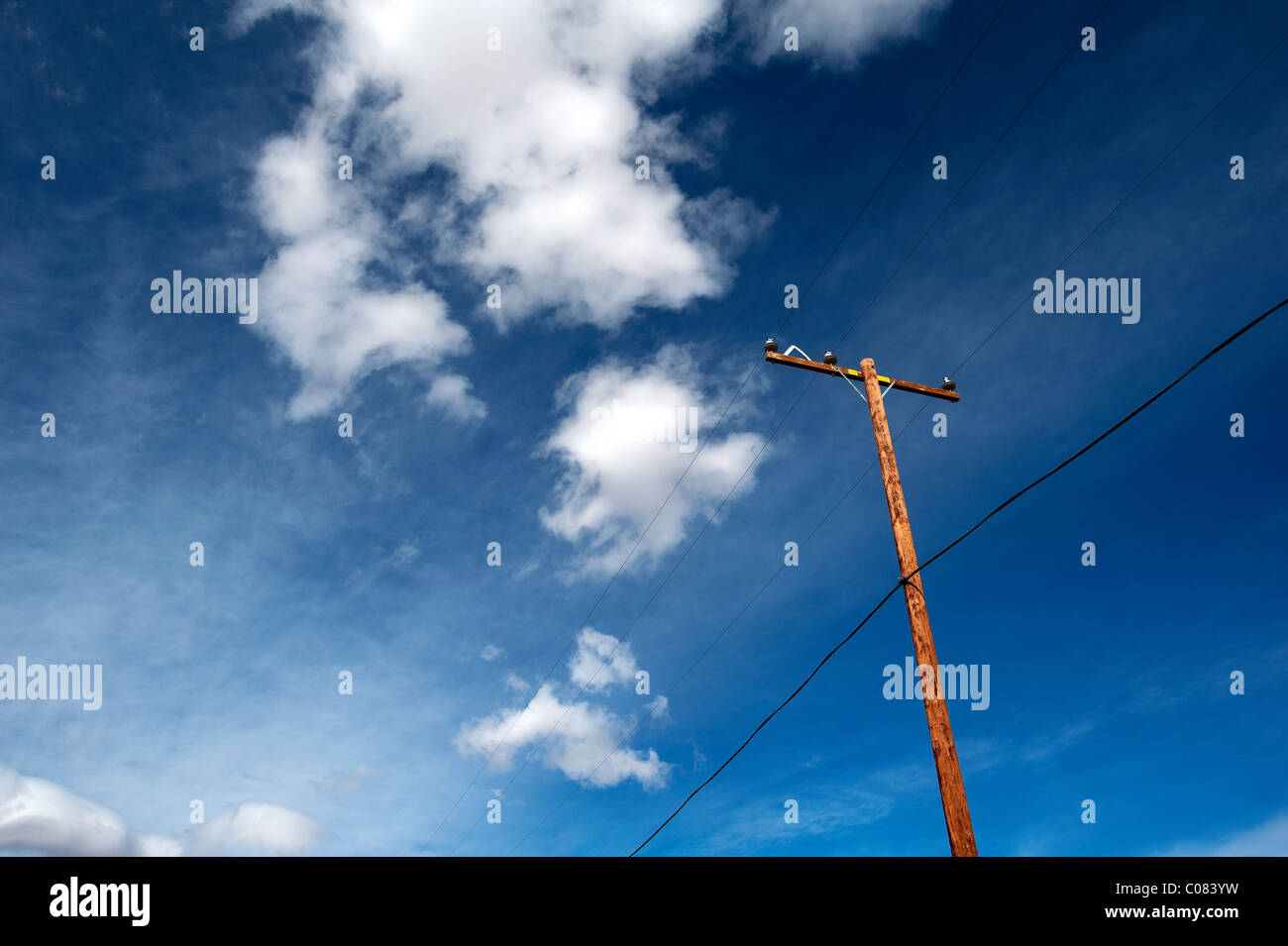 A wooden telegraph pole set against a blue sky with white clouds. California Desert, USA Stock Photo