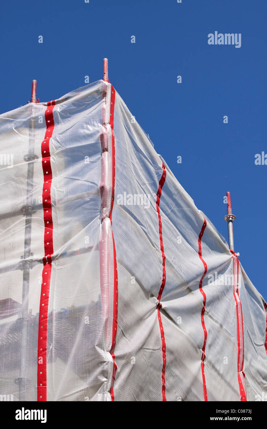 Scaffolding protected with a red and white plastic sheet, construction site, protection from falling parts Stock Photo