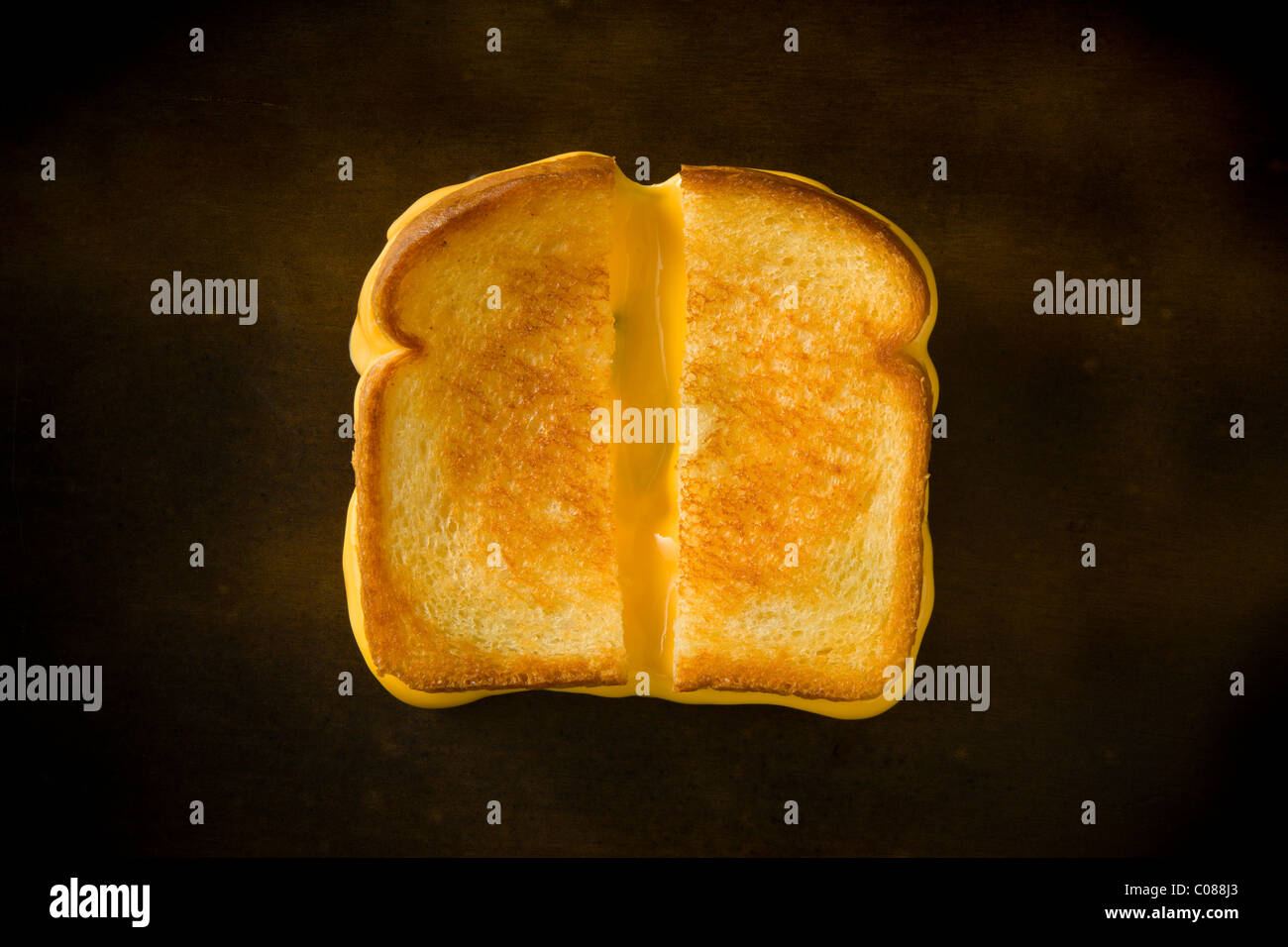 A Grilled Cheese Sandwich cut in half pulling the cheese on a wood table Stock Photo