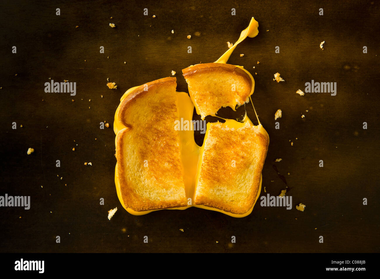 A Grilled Cheese Sandwich cut in half and with the top right corner broken off pulling the cheese on a wood table Stock Photo