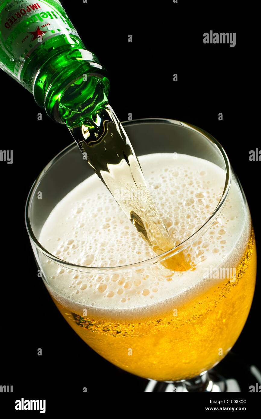 A Bottle of Heineken Beer pouring into a glass on a black background. Stock Photo