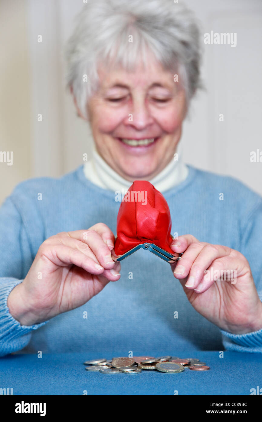 Wealthy senior elderly woman with a pleased expression emptying a pile of money out of a purse in front. England, UK, Britain Stock Photo