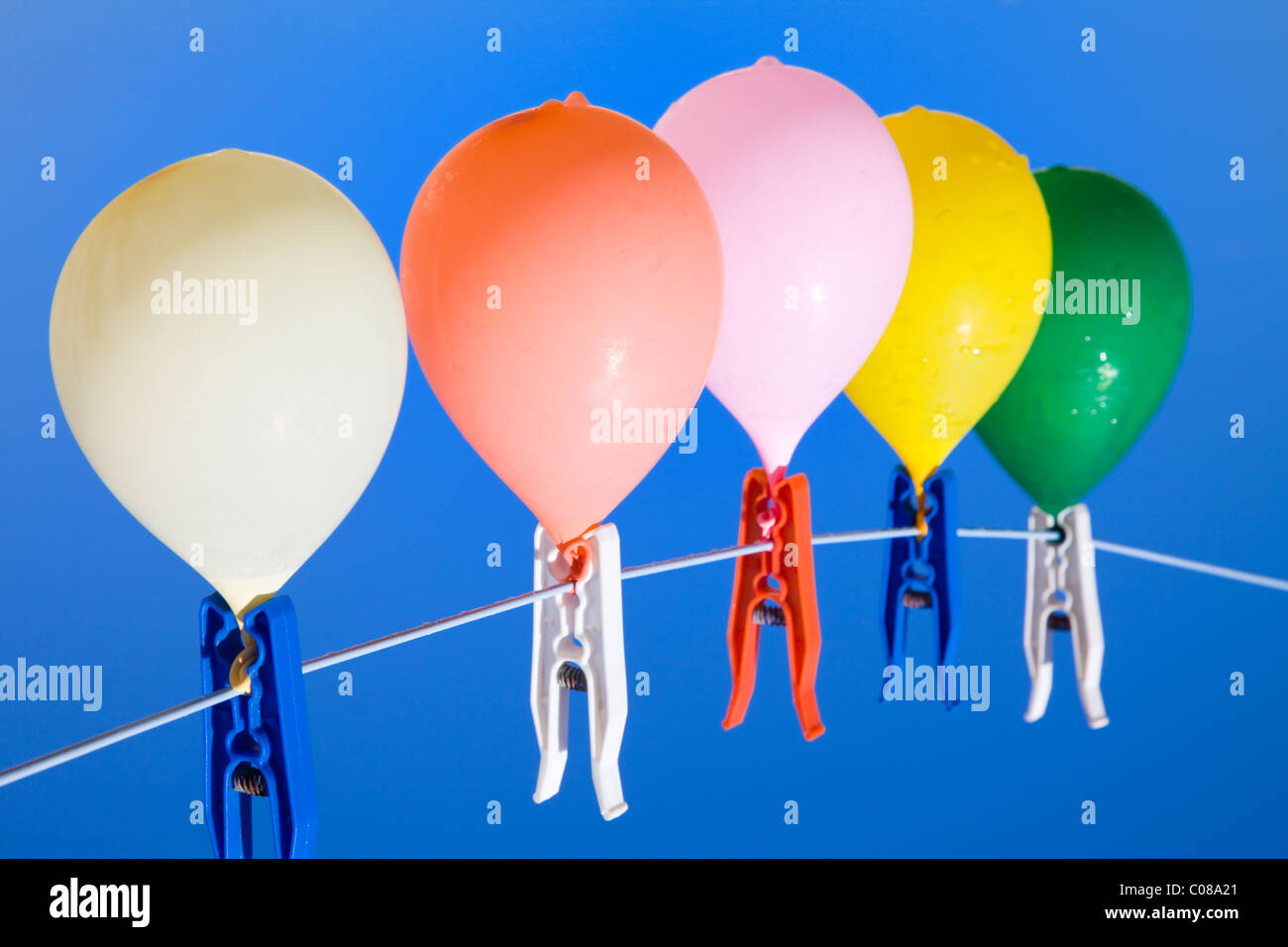 Group of colored water filled balloons hanging on a clothesline with a blue sky as background, seen from below Stock Photo