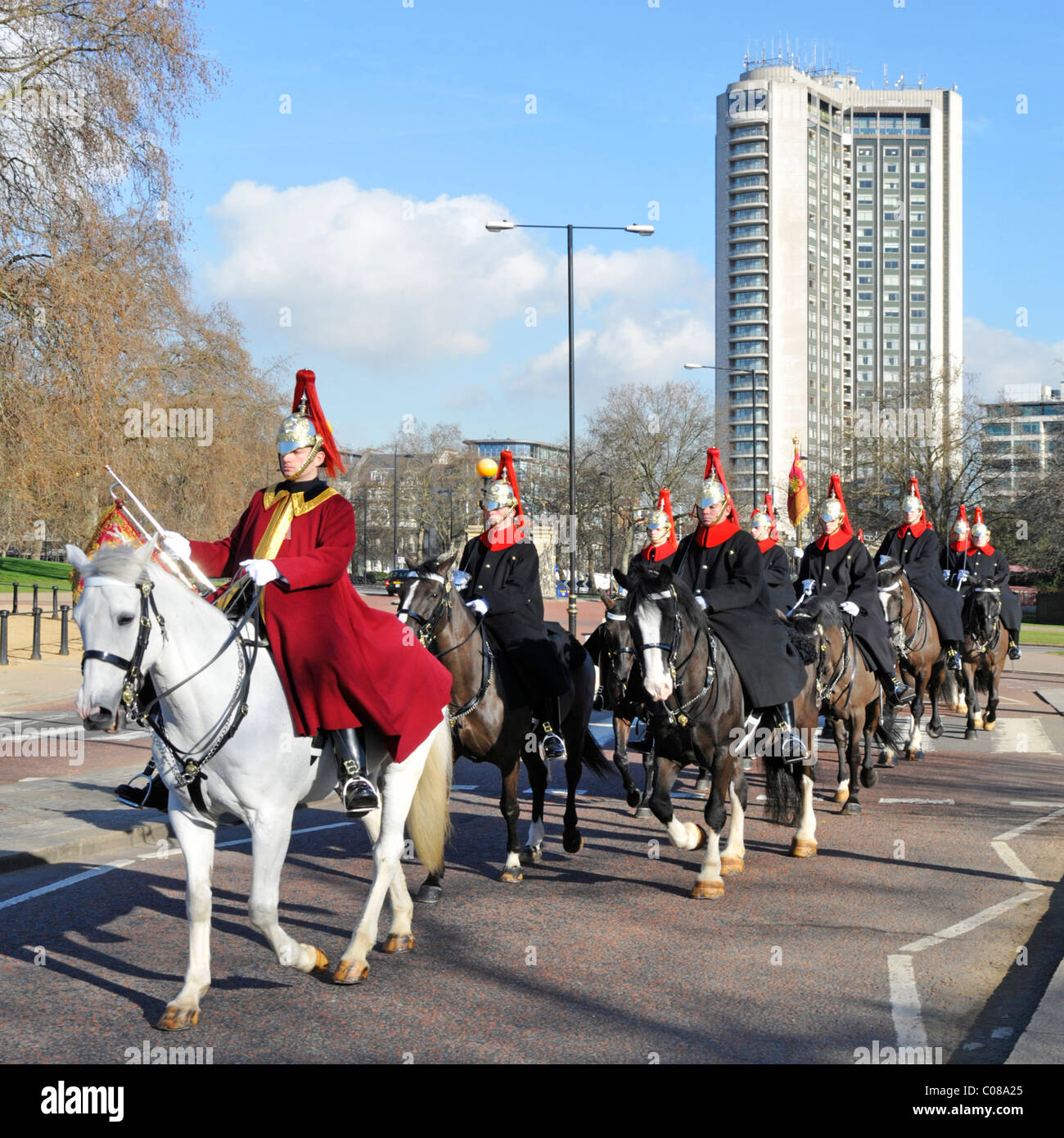 Soldiers & horses of The Blues & Royals mounted regiment Household Cavalry in winter cloaks riding in Hyde Park Hilton Hotel beyond London England UK Stock Photo
