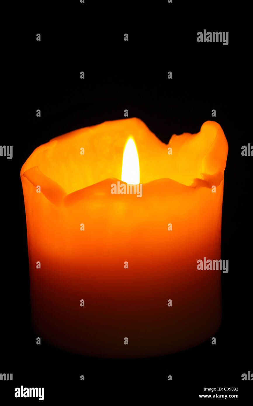 A burning, well used candle with ragged melting edges against a dark background. Isolated. Stock Photo
