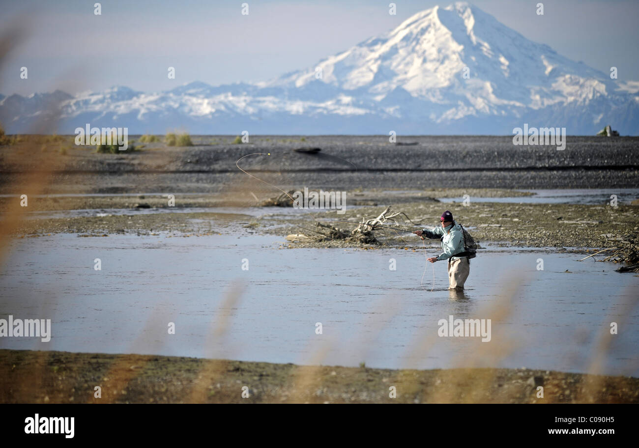 Woman fly fishing for wild Steelhead on Deep Creek with Mt. Redoubt in the background, Kenai Peninsula, Southcentral Alaska Stock Photo