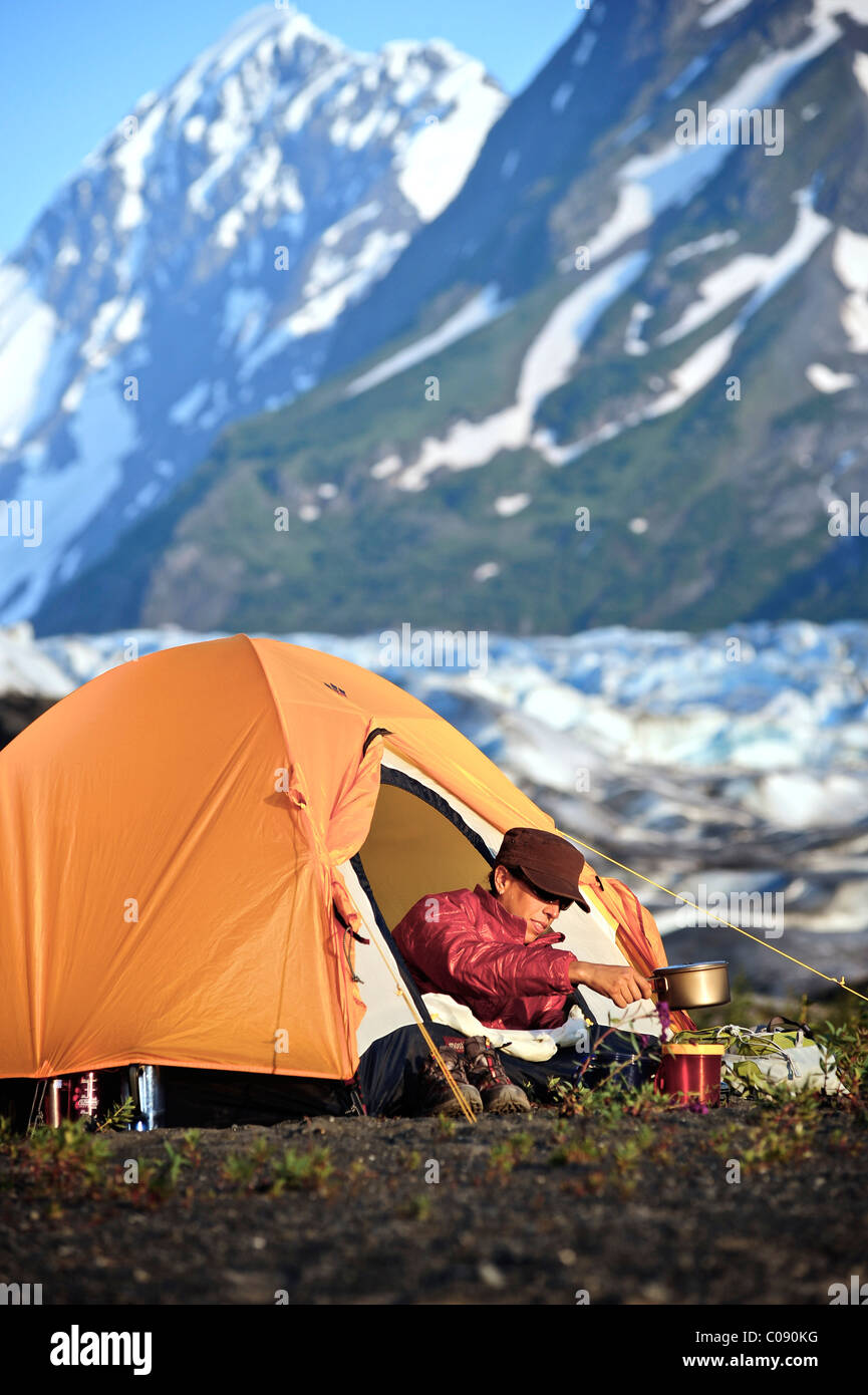 Woman prepares food on a backpacking stove while in her tent, Spencer Glacier in the background, Chugach National Forest, Alaska Stock Photo