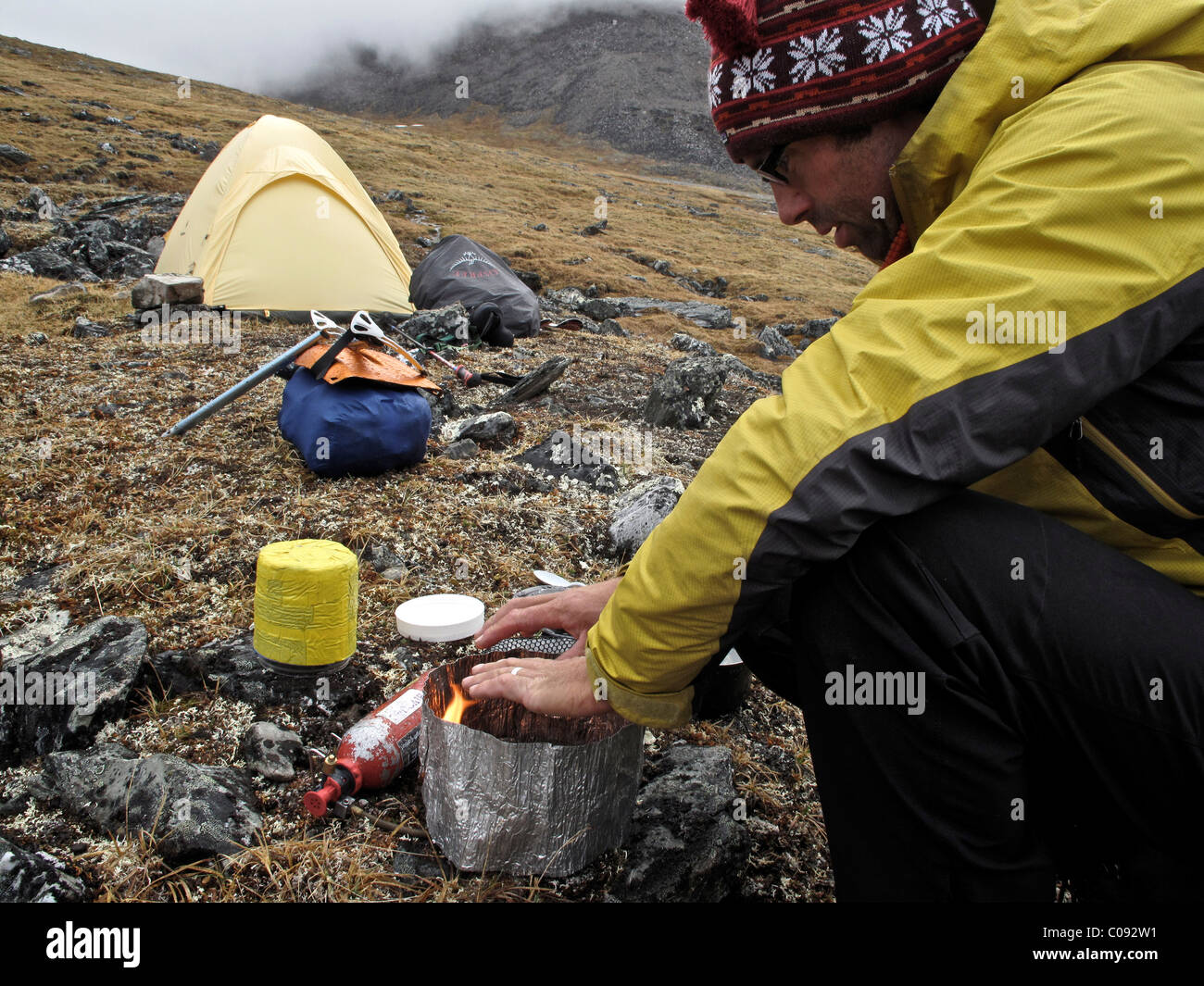 Backpacker prepares food at camp below Mt. Chamberlin, Brooks Range, ANWR, Arctic Alaska, Summer Stock Photo